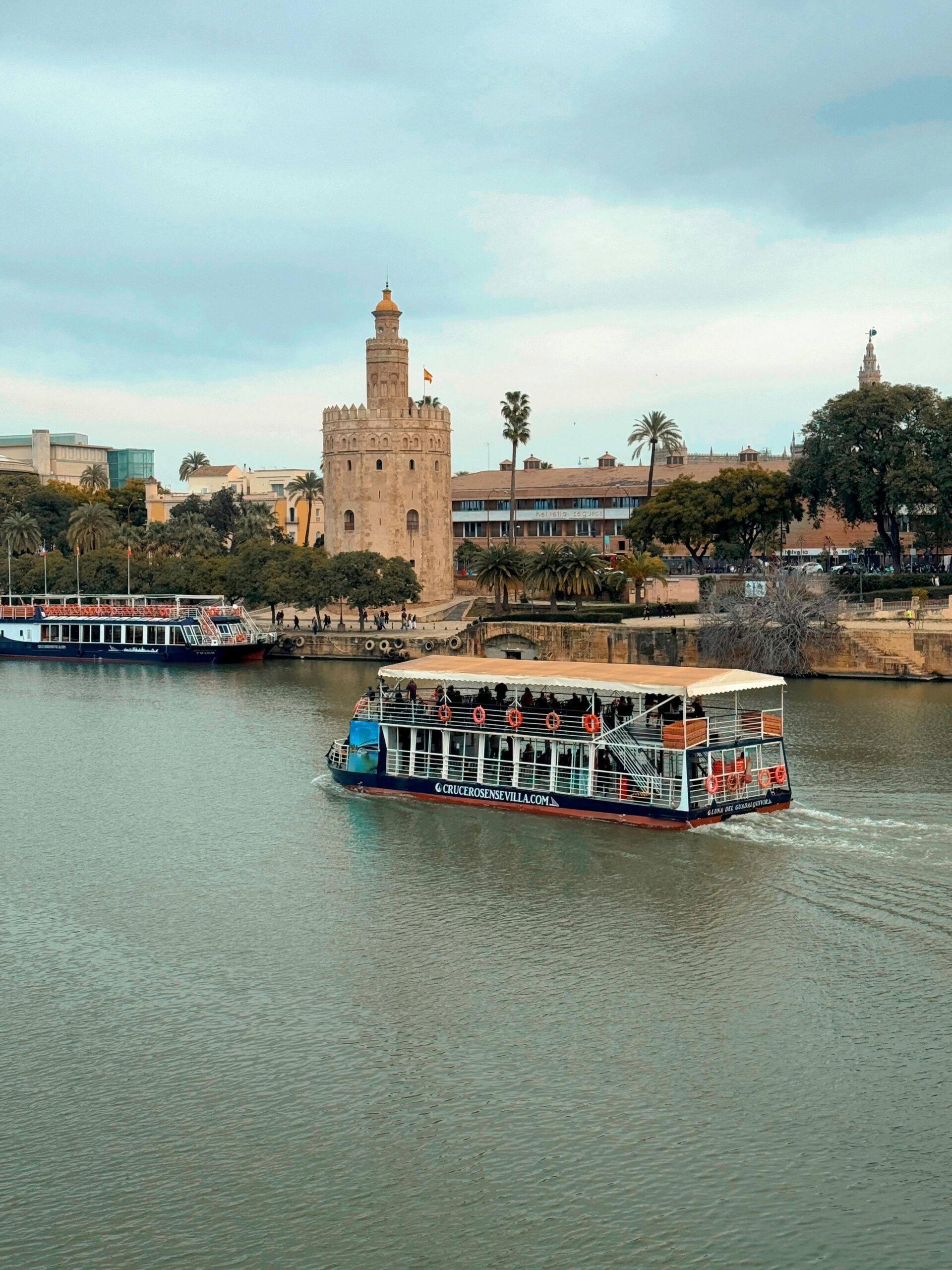 A picturesque boat cruising by the historic Torre del Oro in Seville, Spain.
